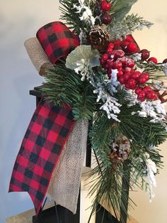 a christmas wreath with pine cones, berries and evergreens on a stand in front of a wall