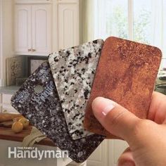 a hand holding four different colored coasters in front of a white kitchen counter top