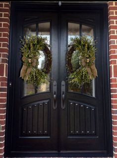 two wreaths on the front door of a brick building with black doors and windows