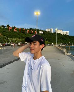 a young man standing in front of the pattaya city sign with his hand on his head