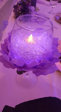 a lit candle in a glass bowl on a table with purple flowers and napkins