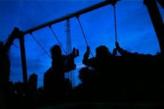 two people sitting on swings at night with the sky in the background