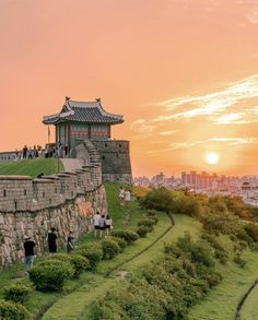 the sun is setting on top of an old wall with people walking up and down it