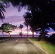 the sun is setting behind palm trees on the side of the road with blurry lights