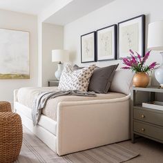 a white bed sitting in a bedroom next to two vases with flowers on them