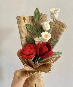 a hand holding a bouquet of crocheted flowers with leaves and ribbons on it