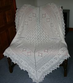 a white crocheted blanket sitting on top of a wooden chair in a room