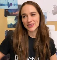 a woman with long brown hair wearing a black t - shirt and smiling at the camera