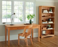 a wooden desk sitting in front of a window next to a book shelf filled with books