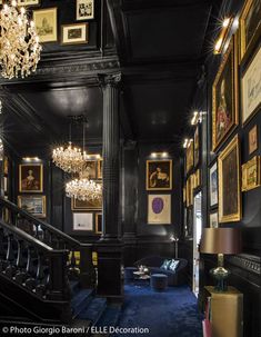 a room with black walls and pictures on the wall, chandelier and blue carpet