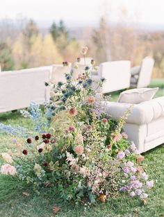 an outdoor ceremony setting with white couches, flowers and greenery in the foreground