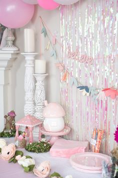 a table topped with lots of pink and white balloons next to a wall covered in confetti