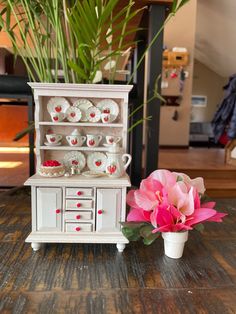 a white china cabinet with pink flowers on the side and a potted plant next to it