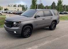 a silver suv parked in a parking lot next to other cars and trees on the side of the road