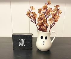 a white vase filled with dried flowers next to a sign that says boo on it