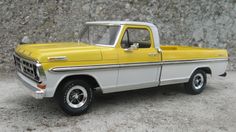 a yellow and white truck parked in front of a rock wall