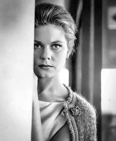 a black and white photo of a woman leaning against a wall looking at the camera