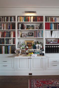 a living room filled with lots of books on top of white bookcases next to a rug