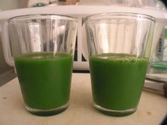 two glasses filled with green liquid sitting on top of a counter