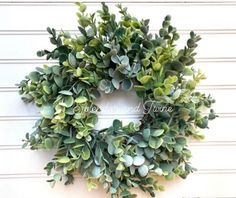 a green wreath hanging on the side of a white wall with greenery around it