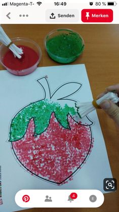 a child's drawing of a strawberry with green and red colors on paper next to two small bowls