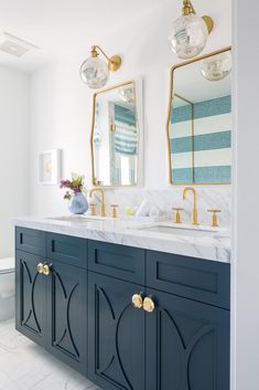 a bathroom with marble counter tops and blue cabinetry, two mirrors above the sinks