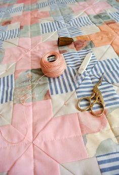 scissors, thread and spools are laying on a quilted tablecloth with pink and blue squares