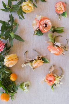 oranges and pink flowers are arranged on a white surface with greenery around them