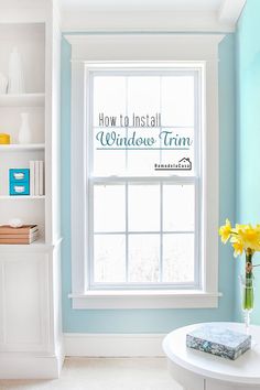 a room with blue walls and white trim on the windowsill, bookshelf in the background