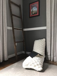 a ladder leaning against the wall next to a white bed in a room with gray walls