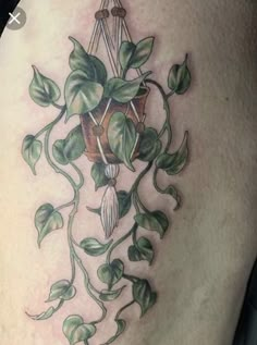 a tattoo on the back of a woman's thigh with green leaves and flowers