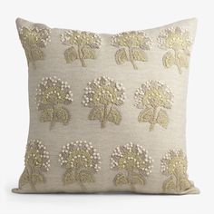 an embroidered pillow with white and green flowers on the front, sitting on a white surface