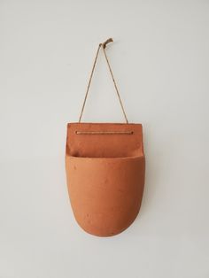 a clay pot hanging from a rope on a white wall with a hook in the middle