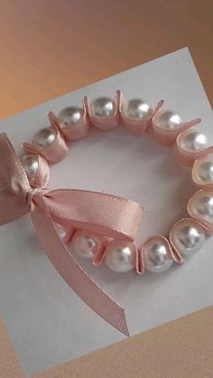 a pink ribbon and pearls bracelet on top of a piece of paper with a bow