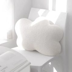 a white cloud shaped pillow sitting on top of a chair next to an open book