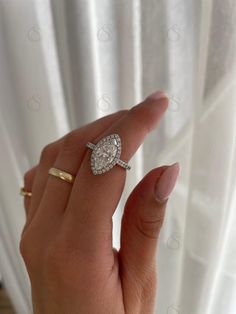 a woman's hand with a diamond ring on top of her finger, in front of a white curtain