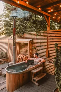 a man sitting in a hot tub on top of a wooden deck next to a fire pit