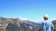 a man standing on top of a mountain looking at the mountains in the distance with snow capped peaks behind him