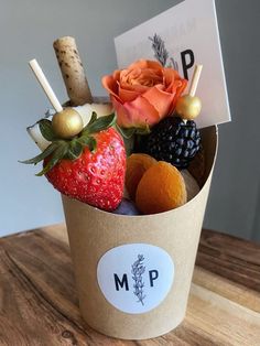 a cup filled with fruit and flowers on top of a wooden table next to a sign