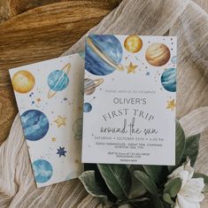 two outer space themed baby shower cards on a blanket with flowers and greenery next to them