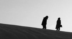 two people standing on top of a sand dune