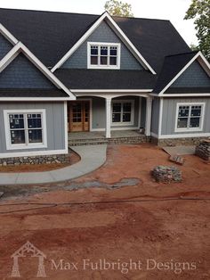 a large gray house with white trim on the front and side windows, surrounded by red dirt