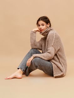 a woman is sitting on the floor wearing a sweater and jeans with her hand under her chin