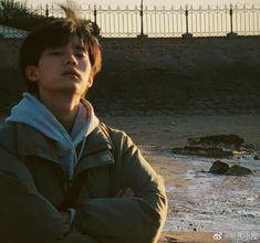 a young man standing on top of a beach next to the ocean with his arms crossed