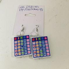 two pairs of earrings with colorful designs on them sitting next to a card game keychain