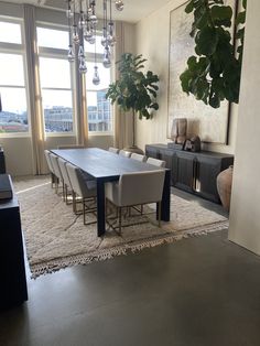 a dining room table and chairs in front of a large window with potted plants