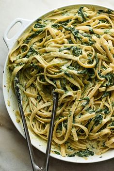 pasta with spinach and pesto in a white bowl next to two serving utensils