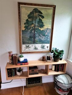 a wooden shelf with books and plants on it in front of a framed tree painting