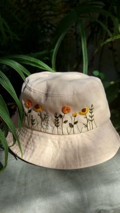 a white hat with yellow flowers on it sitting next to some green plants and leaves