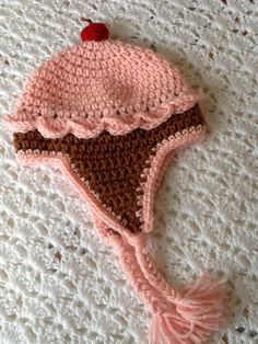 a crocheted hat with a cherry on the top is laying on a white surface